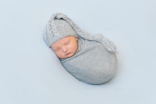 Adorable sweet baby with knitted gray hat on napping wrapped up, curled on his side