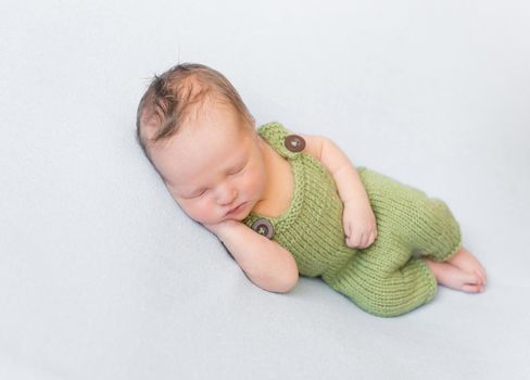 Cute hairy infant wearing summer green knitted costume, sleeping with his hand under the cheek