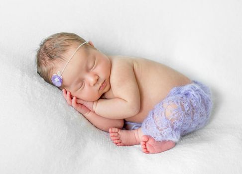 lovely sleeping newborn girl with hands under head in violet knitted panties