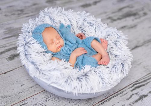 lovely infant in hat and jumpsuit sleeping on round little bed, top view