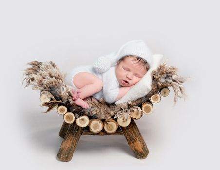 Charming newborn baby asleep on belly curled up on wooden crib. Lovely newborn in grey soft outfit