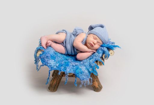 Little infant boy sleeping on his side with his hand under cheek. Baby lying on wooden crib covered with blue rug
