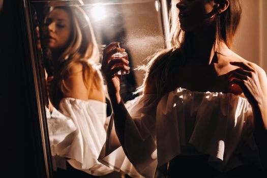 A young woman in an evening dress with perfume stands in front of the home dressing table.The girl uses perfume before going to a party