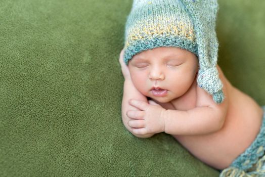 funny newborn baby in knitted hat sleeping with opened mouth on green blanket