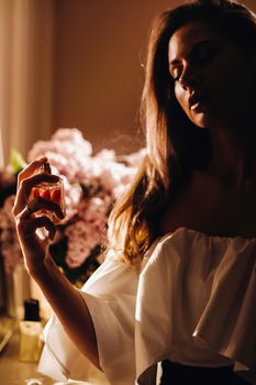 A young woman in an evening dress with perfume stands in front of the home dressing table.The girl uses perfume before going to a party