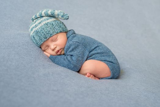 sleeping newborn baby in blue knitted jumpsuit and hat with crossed legs