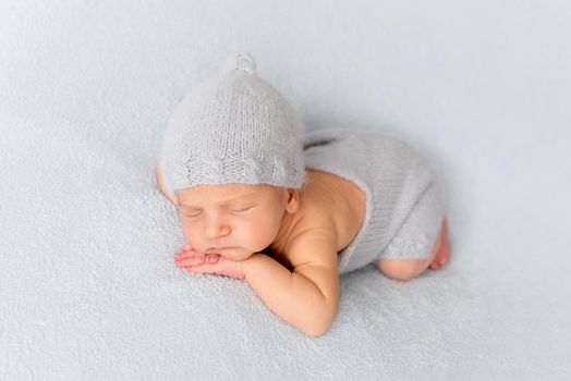 Tender little baby comfortably sleeping on belly. Newborn in tushy up pose on white blanket