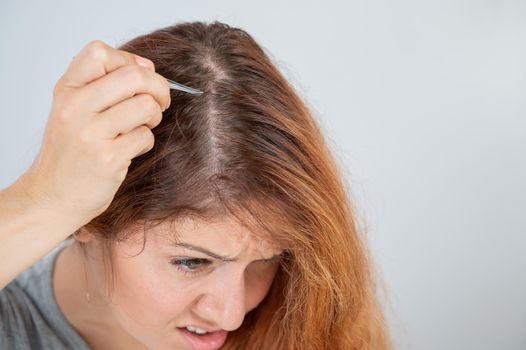 Caucasian woman finds gray hair and removes it with tweezers. Signs of aging