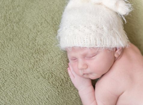 lovely newborn baby in knitted hat sleeps curled up, top view