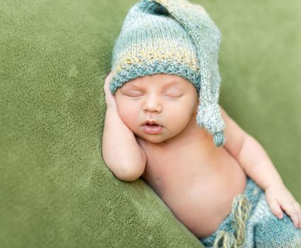 funny newborn baby in knitted hat sleeping with opened mouth on green blanket