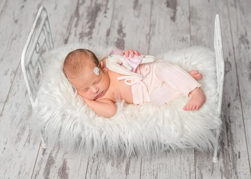 newborn sleeping baby in panties holding toy on cute little bed with white fluffy blanket