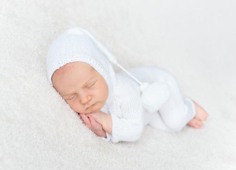 Adorable infant boy in white bodysuit sleeping on tummy on a light blanket
