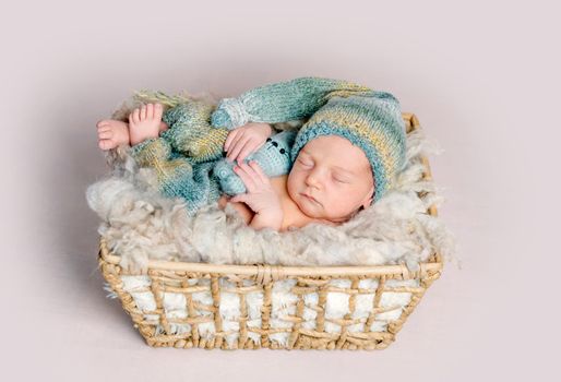 Newborn baby sleeps in a box on a fluffy background in a photo studio, top view. Newborn sleeps with toy in hands