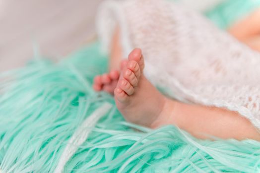 tender newborn baby legs on fluffy colorful blanket, closeup