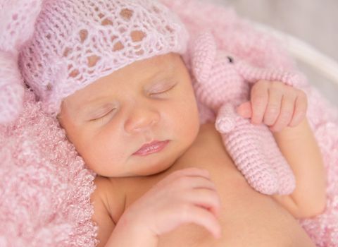 lovely newborn girl in pink panties and hat, with toy in basket on wooden background, top view