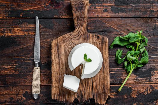 Fresh Ricotta cream Cheese on wooden board with basil. Dark wooden background. Top view.