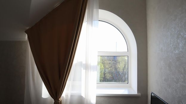 Arched window in the living room with tulle and curtain. Modern and bright bedroom interior