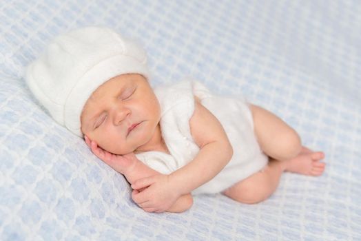 cute sleeping on hand newborn in white romper and hat on a blanket