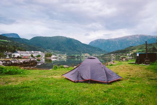 Norwegian fjord landscape with camping tent. Norway adventure. Camping tent at scenic wild fjord, a lake shore with mountain range in background - Norway.