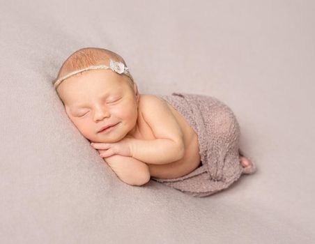 smiling sleeping newborn girl with hands under her head covered with knitted shawl