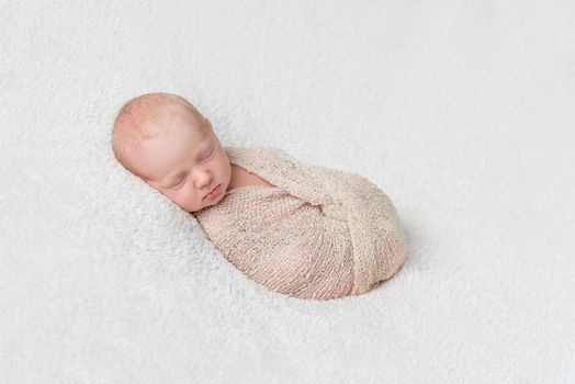 lovely sleeping baby wrapped in beige diaper on white blanket