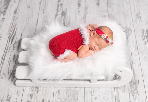 beautiful newborn in red romper sleeping on sleigh cot with white fluffy blanket