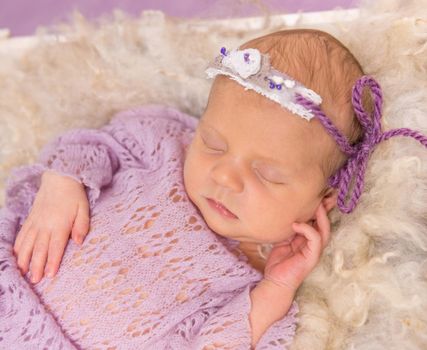 sweet newborn girl sleeping in square cot on violet background and cute hat with costume