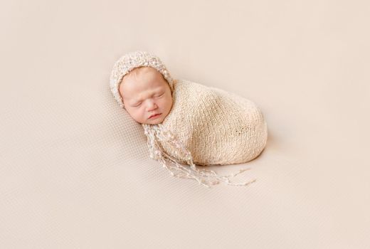 lovely wrapped newborn baby in knitted hat sleeping on a beige blanket