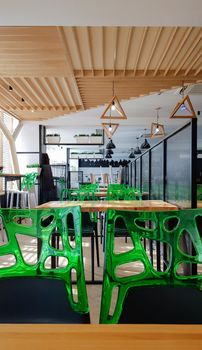 Cafeteria, no people dining room with wooden tables and green chairs. Interior with wood and metal elements. Modern dining areas with window lighting. Ukraine, Kiev - February 19, 2021.