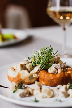 Stuffed mushrooms filled with cheese, mushroom stem and microgreen on the white plate with a glass of wine in the restaurant