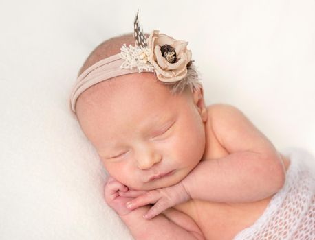 Cute sleeping newborn girl in flower band. Dreamy girl sleeping happily on white plaid