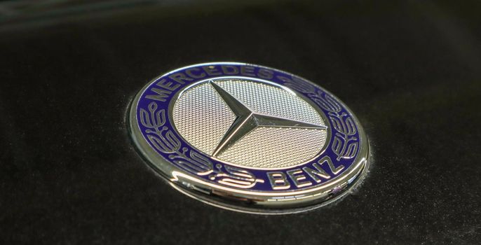 Close-up of the blue circular Mercedes Benz logo on the hood of a black car after polishing with highlights. The concept of a modern luxury sedan and European car. Ukraine, Kiev - June 09, 2021