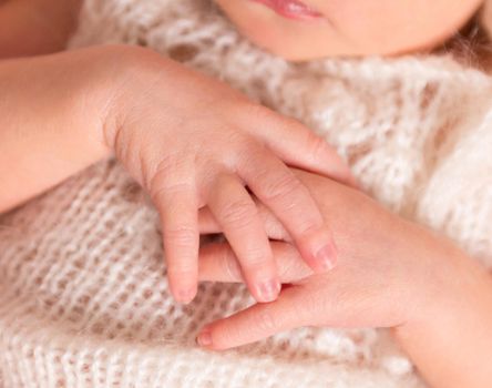 little tender hands of newborn baby on knitted peachy suit, closeup