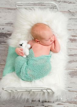 lovely wrapped newborn sleeping on cot with white soft blanket and toy