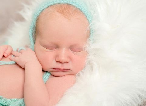 funny asleep baby face in hat on soft white blanket, closeup