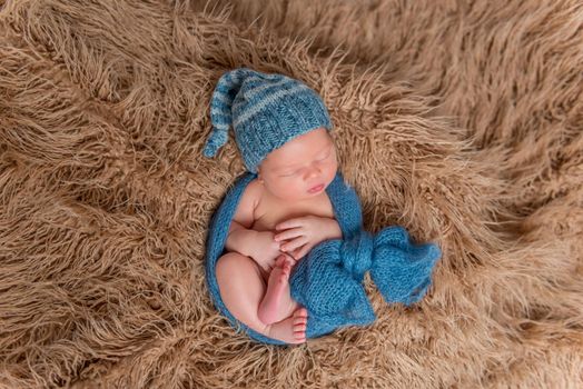 Newborn dressed in a hat and wpapped in scarf, sleeping on a fluffy blanket, topview