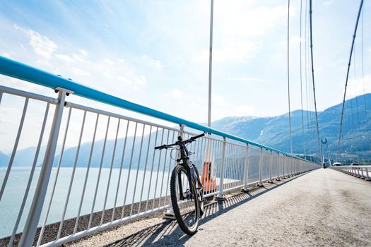 Theme of mountain biking in Scandinavia. human tourist in helmet and sportswear on bicycle in Norway on Hardanger Bridge suspension bridge thrown across the Hardanger Fjord in southwestern Norway.