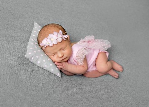 Lovely newborn girl in pink dress sleeping with pillow under her little head. Little princess with flowery hair band sleeping on her side