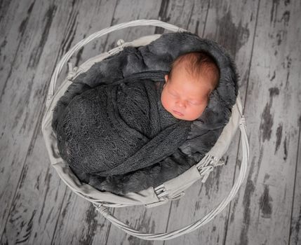 Lovely newborn wrapped in a tight dark blanket sleeping in a small grey cradle