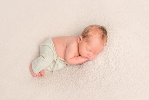 Curled up chubby baby in tiny white pants, sleeping on a carpet, topview