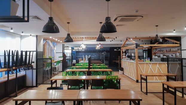 Cafeteria, no people dining room with wooden tables and green chairs. Interior with wood and metal elements. Modern dining areas with window lighting. Ukraine, Kiev - February 19, 2021.
