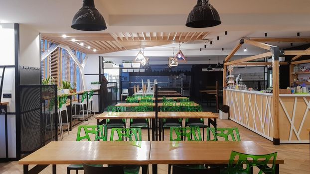 Cafeteria, no people dining room with wooden tables and green chairs. Interior with wood and metal elements. Modern dining areas with window lighting. Ukraine, Kiev - February 19, 2021.