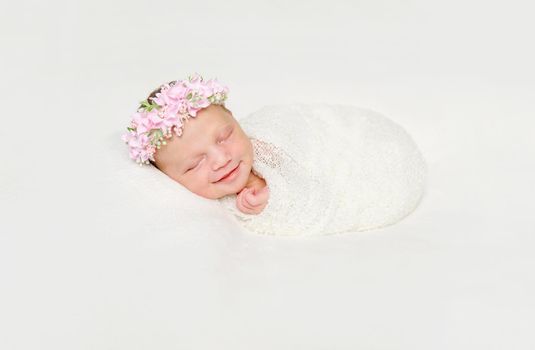 cute newborn baby swaddled in white diaper smiling asleep with flowers on headband