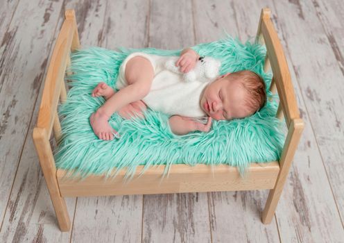 beautiful sleeping baby in jumper on wooden cot with turquoise fluffy blanket