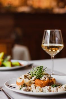 Stuffed mushrooms filled with cheese, mushroom stem and microgreen on the white plate with a glass of wine in the restaurant