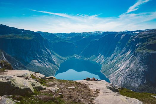 July 26, 2019. Norway. man dreamer lying on stone, relaxing after hiking on cliff mountain top with blue water fjord on background. Norway trip, freedom concept. tourist on top mountain uses phone.