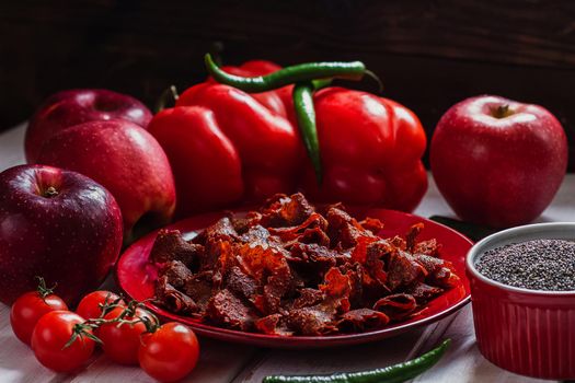 Sun-dried tomatoes with paprikas and chilly peppers on red plate.