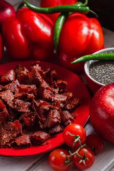 Sun-dried tomatoes with paprikas and chilly peppers on red plate.