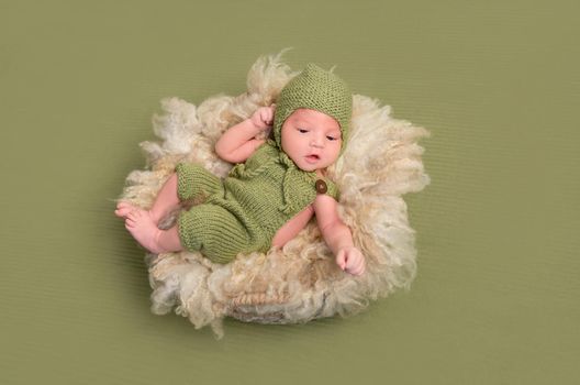 Funny baby in knitted costume in a lovely pose, resting on a furry big pillow