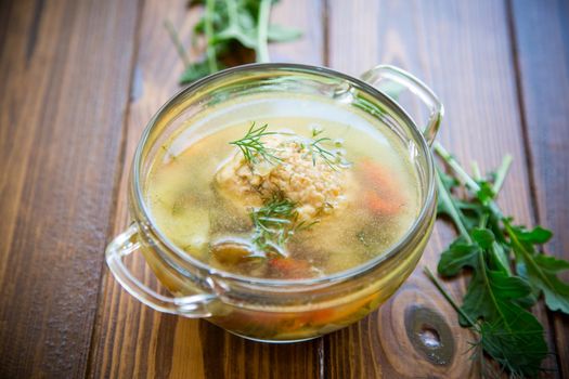 fresh hot soup with chicken meatballs and vegetables in a plate on a wooden table
